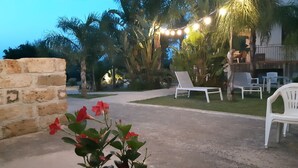 Un espace extérieur aménagé en terrasse, avec des chaises en plastique blanches, un mur de briques et des guirlandes lumineuses.