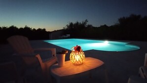 Une piscine au crépuscule, avec quelques chaises et une table sur laquelle se trouve une lampe.