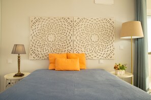 Ein ordentlich eingerichtetes Schlafzimmer mit einem großen Bett, einer Wandverkleidung, einer Nachttischlampe und einem kleinen Tisch mit einer Pflanze.