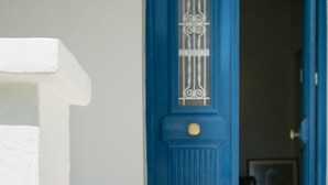 Eine blaue Tür mit einem dekorativen Glasfeld und einer kleinen runden Lampe darüber.