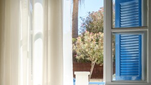 Ein Schlafzimmer mit Bett, einem Fenster mit blauen Rollläden und Blick auf einen Garten.
