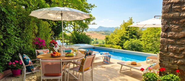 Ein Poolbereich mit Holzdeck, Sitzgelegenheiten im Freien und Blick auf die Landschaft.