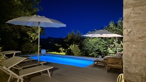 Ein Pool im Freien mit Liegestühlen und Sonnenschirmen, umgeben von Bäumen und einer Bergkulisse.