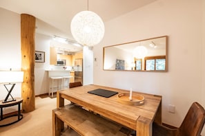 A modern dining area with a wooden table, bench, and pendant light. A kitchen is visible in the background. - Ski in/out | BBQ | Complex pool & Hot tub | Garage (Whistler)