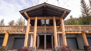 A building with a wooden balcony, stone pillars, and a staircase leading to the entrance. - Ski in/out | BBQ | Complex pool & Hot tub | Garage (Whistler)