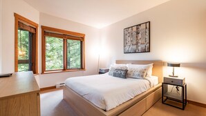 A bedroom with a bed, bedside tables, a desk, and a window with a view of trees. - Ski in/out | BBQ | Complex pool & Hot tub | Garage (Whistler)