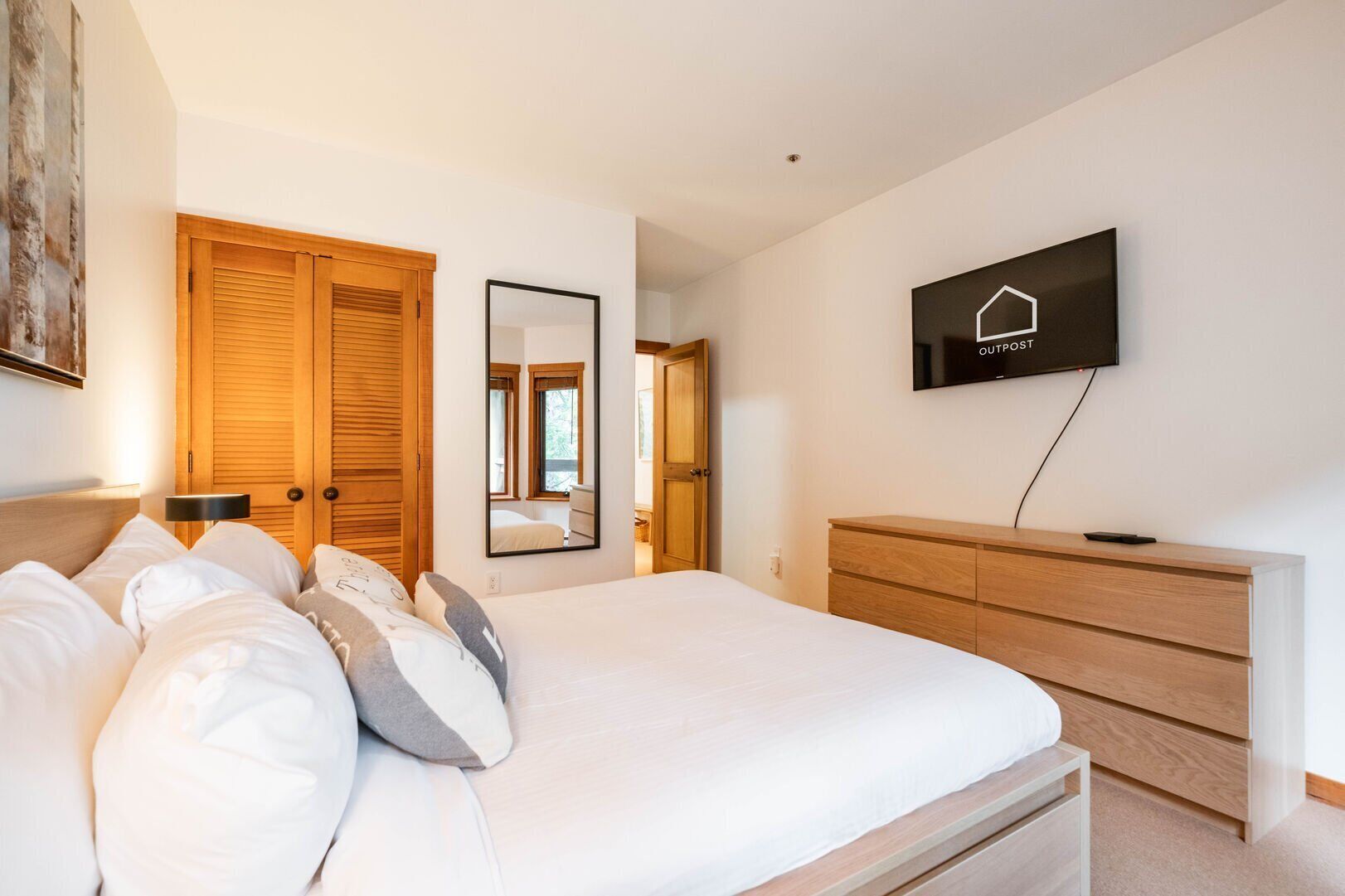 A bedroom with a bed, wooden wardrobe, a TV, and a mirror.