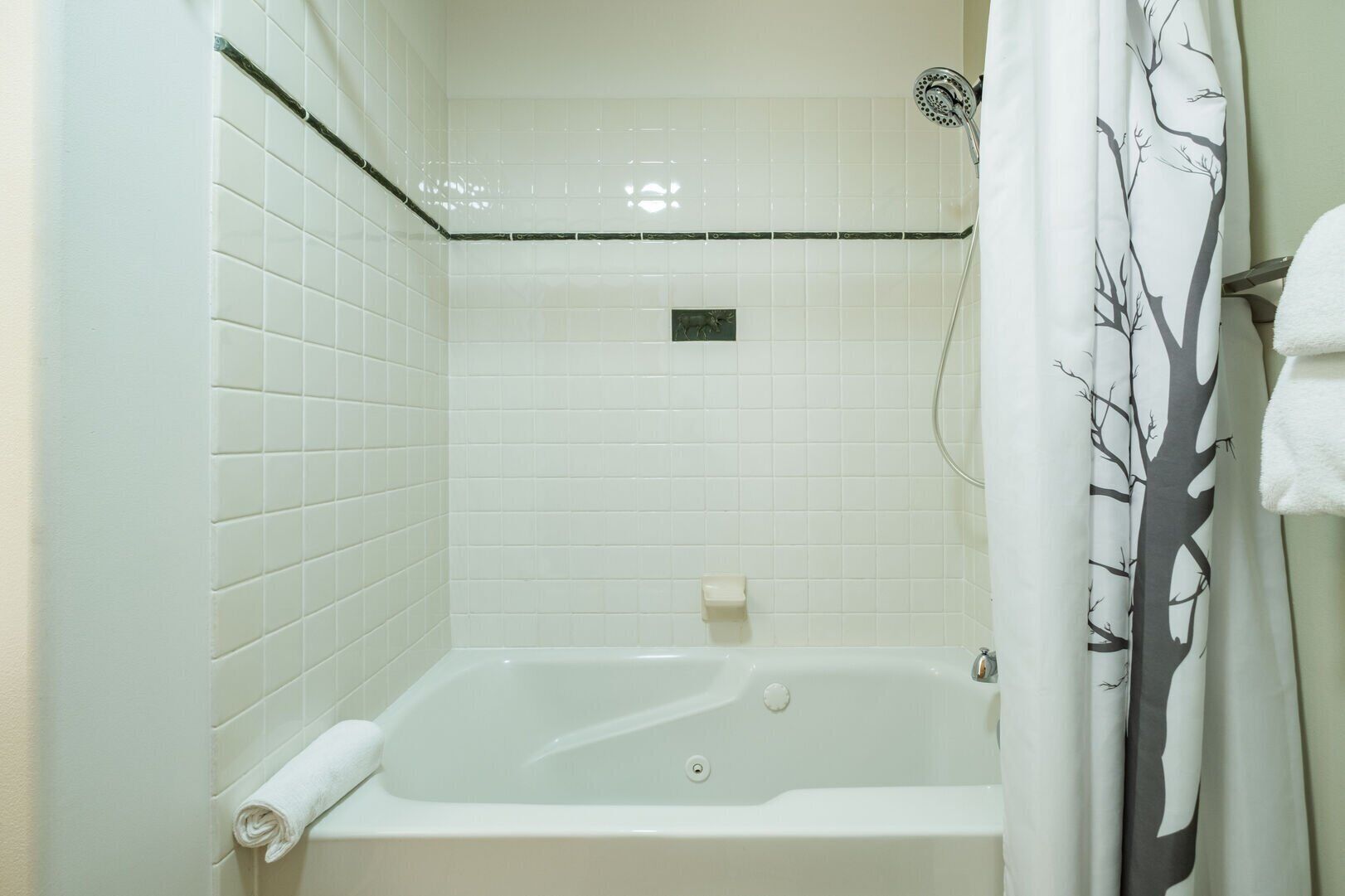 Ein Badezimmer mit weiß gefliesten Wänden, einer Badewanne, einer Duschbrause und einem Duschvorhang mit Baumdekor.