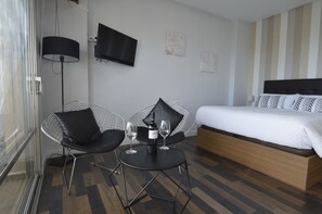 A hotel room with a bed, a TV, a small table with two wine glasses, and a chair.