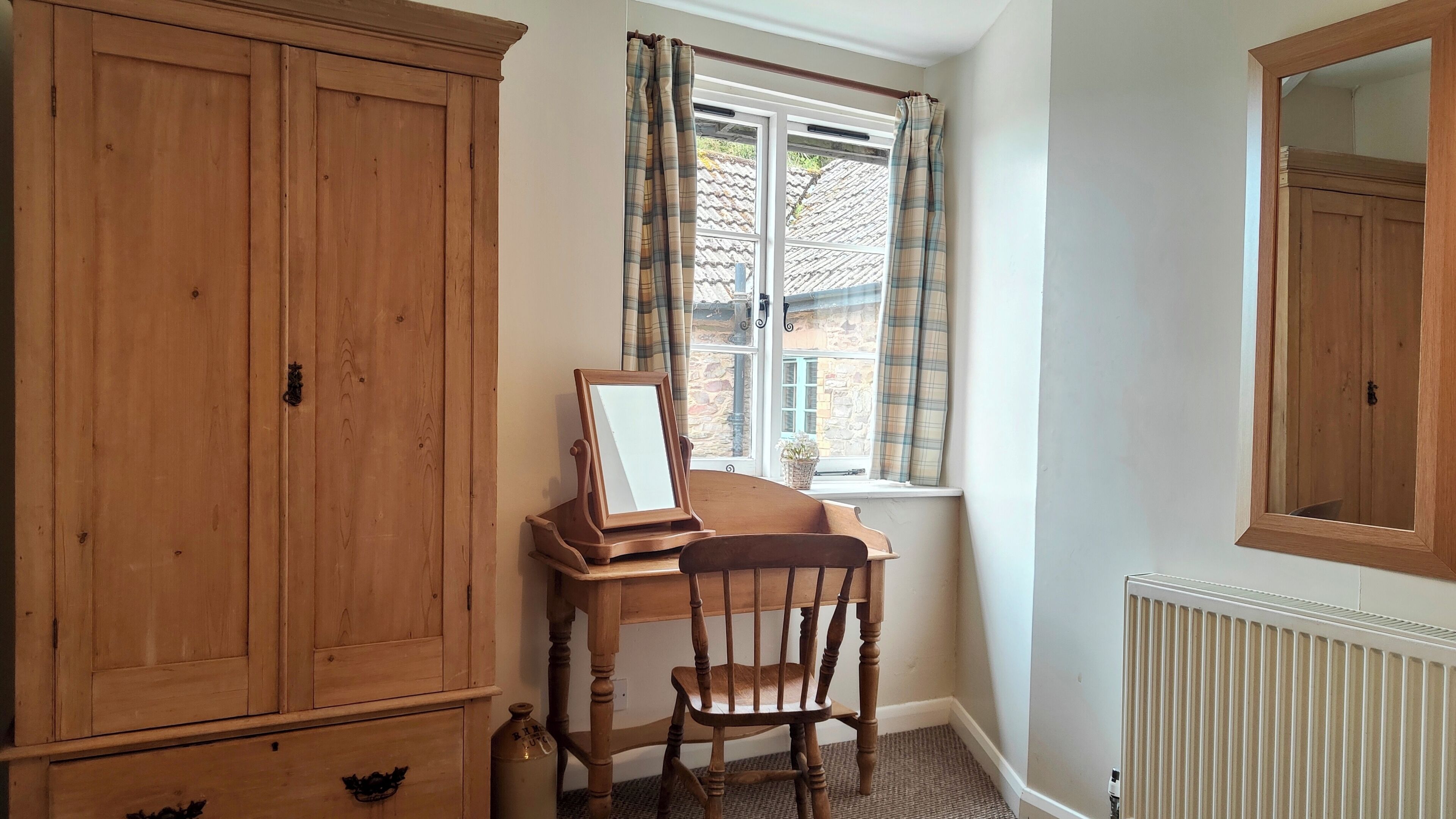 A room with a wooden desk, a chair, a wardrobe, a window with curtains, and a radiator.