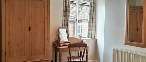 A room with a wooden desk, a chair, a wardrobe, a window with curtains, and a radiator.