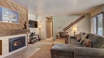 A cozy living room with a fireplace, a sofa, a coffee table, and a TV mounted on the wall.