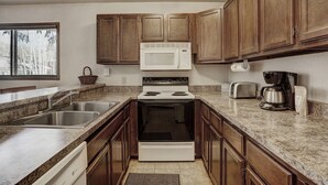 A kitchen with wooden cabinets, a microwave, a stove, a toaster, and a coffee maker. - Ground Floor Condo, Courtyard View, Pool & Hot Tub, Shuttle to Slopes (Keystone)