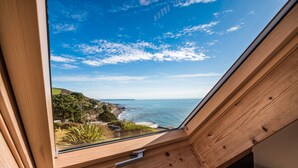 A coastal view from a window with a wooden frame, overlooking a beach and ocean.