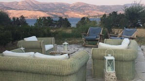 Mobilier d’extérieur en osier disposé sur une terrasse en pierre, offrant une vue sur les montagnes et un plan d’eau.