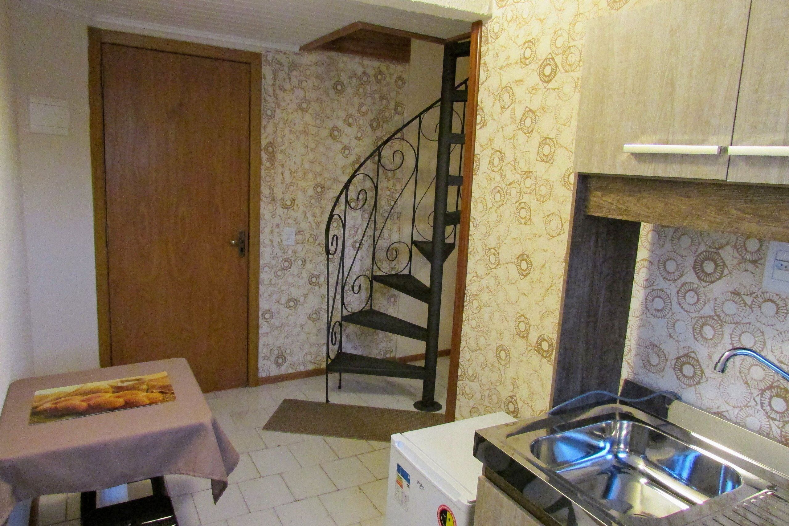 A compact kitchen with a sink, a small table with a placemat, a refrigerator, and a wooden door.