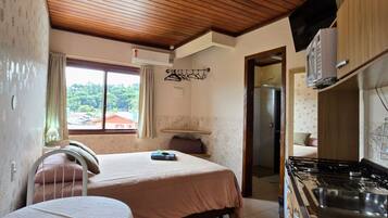 A compact room with a bed, a small table, a kitchenette, and a window with curtains.