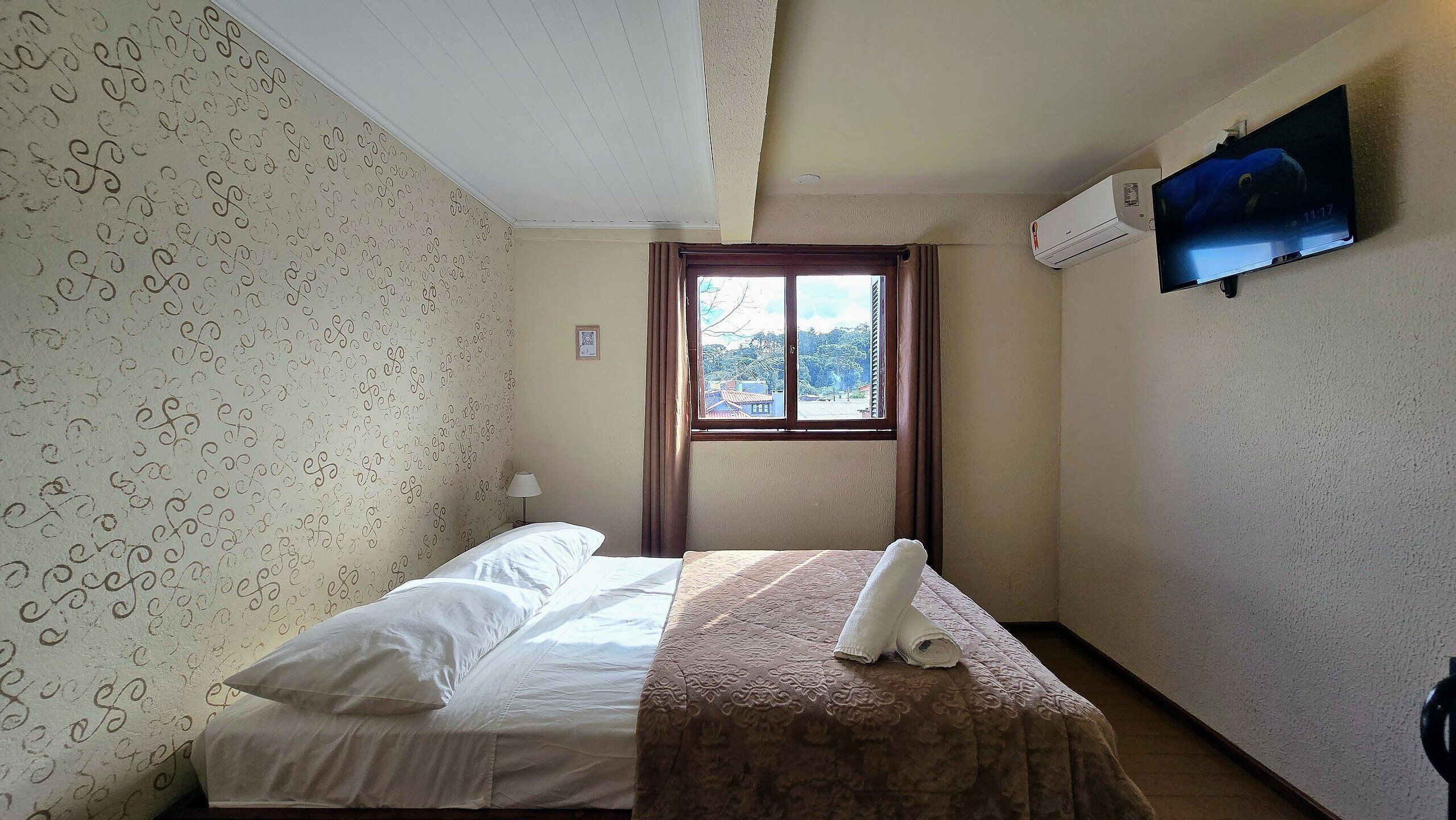Een hotelkamer met een bed, een raam met gordijnen, een tv aan de muur en een airconditioning.