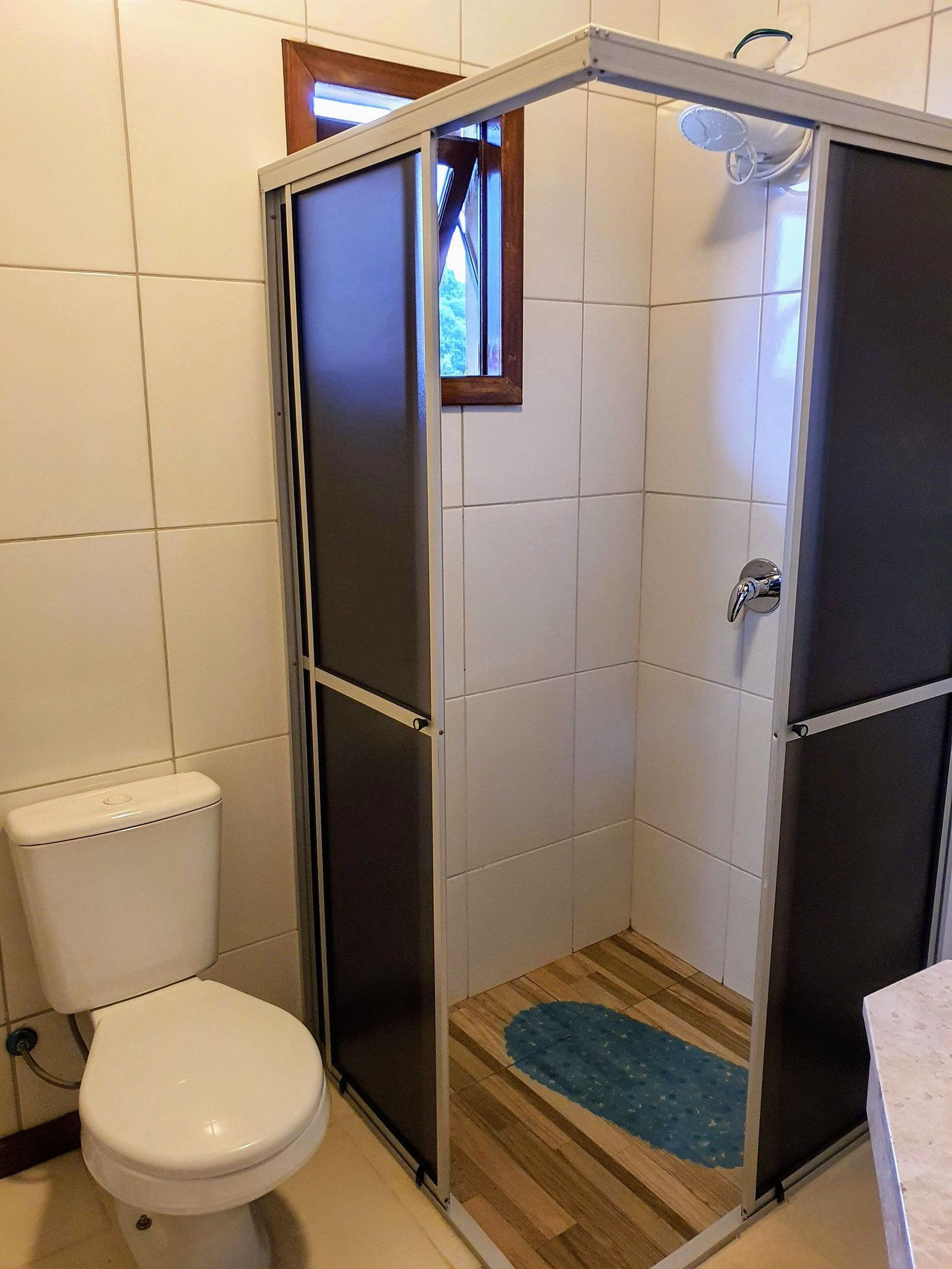 A bathroom with a white toilet, a shower enclosure with a wooden floor, and a small window above the shower.
