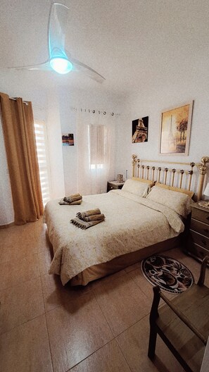 A bedroom with a bed, a nightstand, a chair, a ceiling fan, and a window with curtains.
