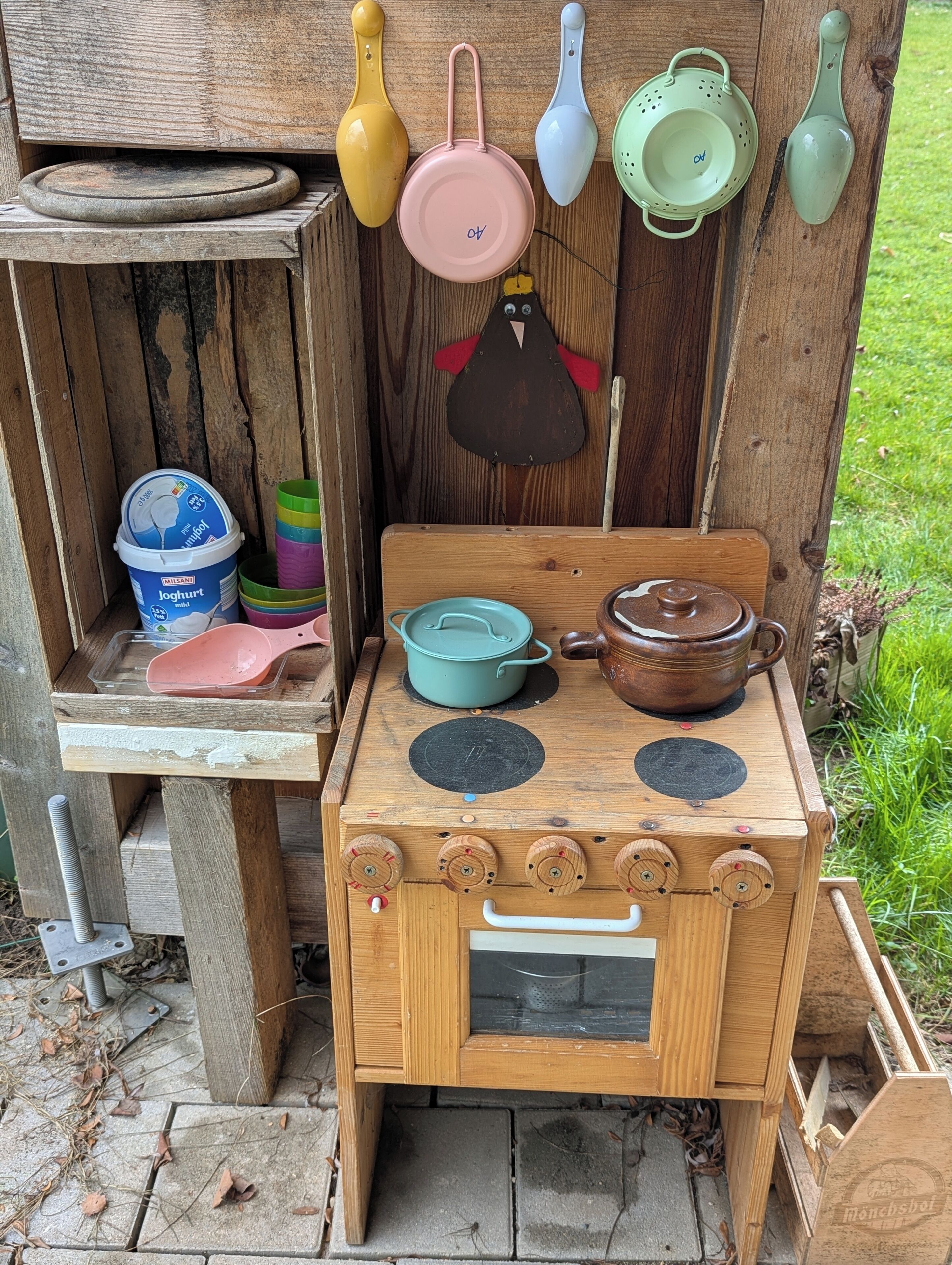 A rustic wooden stove with pots and pans, a small shelf with containers, and a hanging utensil rack.