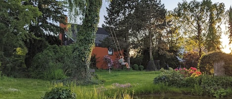A garden with a pond, lush greenery, and a house in the background.