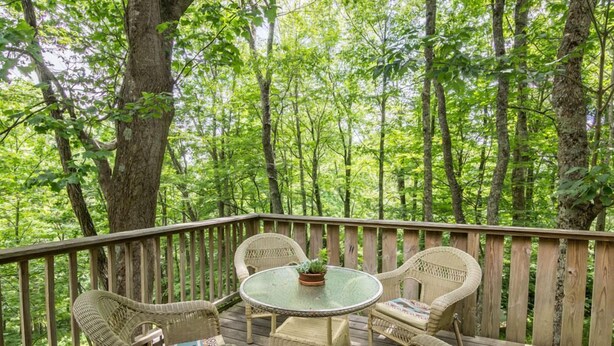 A wooden deck with wicker furniture and a glass table, surrounded by a forest. - A Treetop Escape: All Nights $199! App Ski Mtn home with spacious decks! (Blowing Rock)