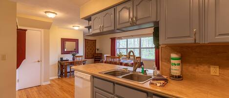 A kitchen with wooden flooring, grey cabinets, a dishwasher, and a window with red curtains.