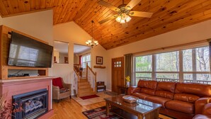 A cozy living room with a fireplace, leather sofa, and a television mounted on the wall. - A Treetop Escape: All Nights $199! App Ski Mtn home with spacious decks! (Blowing Rock)