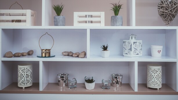 A neatly organized shelf with various decorative items including planters, candles, and a heart-shaped ornament. - Feel in Sarajevo Apartment + Parking (Sarajevo)