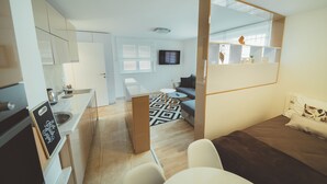 A modern hotel room with a kitchenette, a sofa, a TV, and a large mirror. - Feel in Sarajevo Apartment + Parking (Sarajevo)
