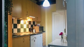Una cocina compacta con armarios de madera, microondas y cafetera. Hay una mesa de comedor con una silla y un florero con flores.