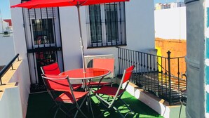 Un balcón con una sombrilla roja, una mesa y dos sillas.