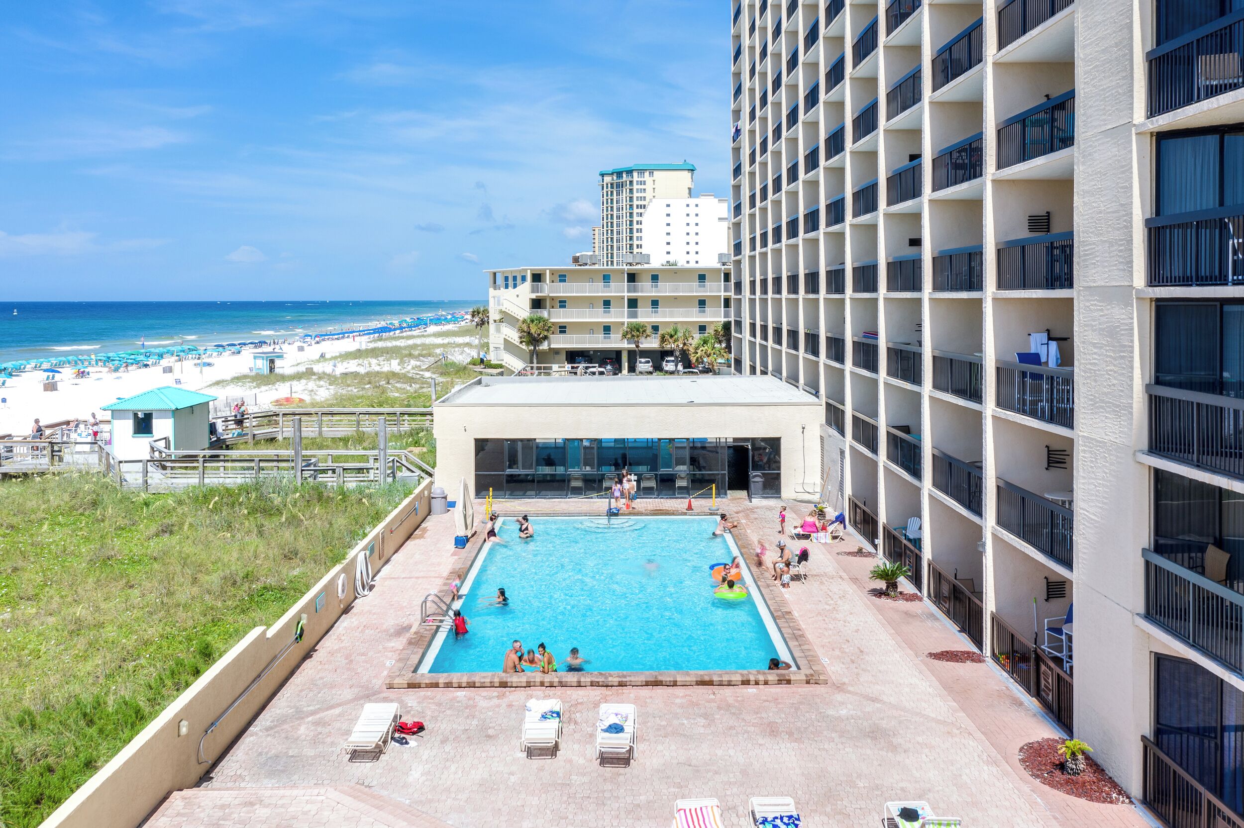 A rooftop pool with a view of the beach and ocean, surrounded by a building with multiple balconies.