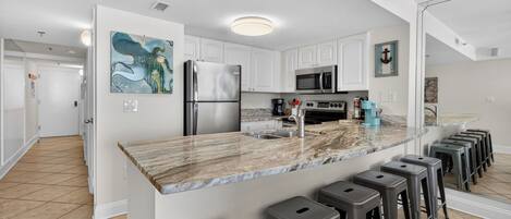 A modern kitchen with white cabinets, a stainless steel refrigerator, a microwave, and a marble countertop.