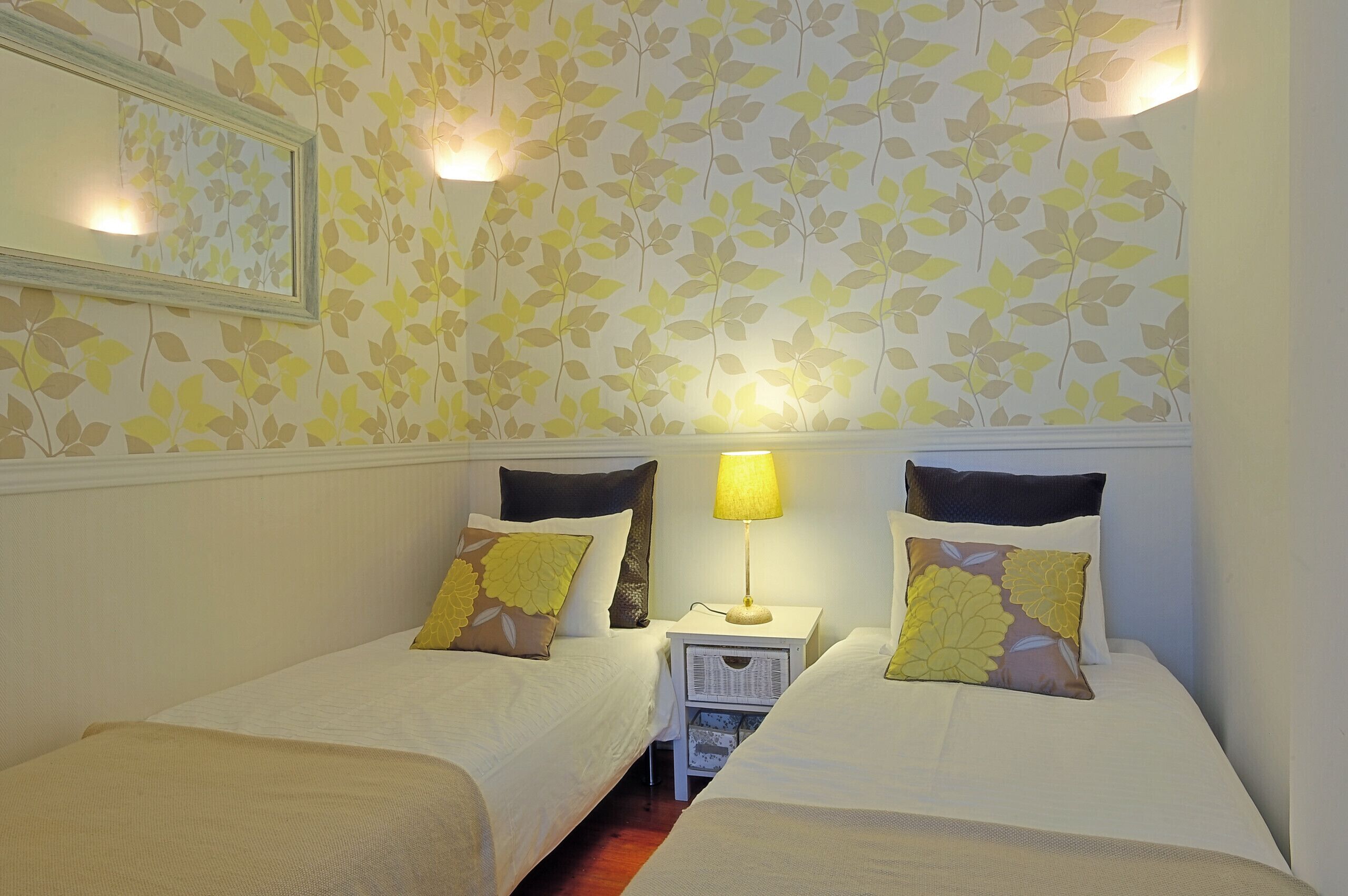Een kamer met twee bedden, een nachtkastje met een lamp en een spiegel aan de muur.