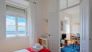A bedroom with two beds, a window with a view, a desk with a TV, and a dining area with chairs and a table. - RM3 - River View | Alfama | AC | 4BR | 3 BATH Sleeps 9 (Lisbon)