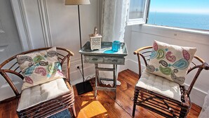 A room with two wicker chairs, a small table with a lamp, and a view of the sea. - RM3 - River View | Alfama | AC | 4BR | 3 BATH Sleeps 9 (Lisbon)
