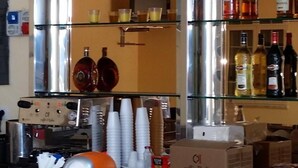 En bardisk med rostfria vitvaror, en kaffemaskin och hyllor med flaskor och koppar.