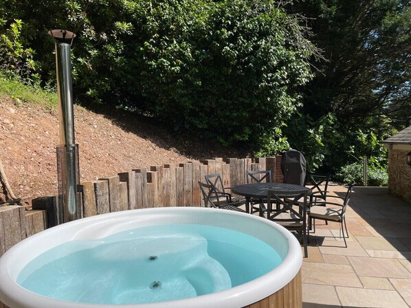 A hot tub with a wooden table and chairs, surrounded by a wooden fence and trees.