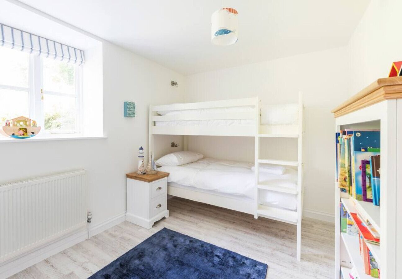 A child's bedroom with bunk beds, a nightstand, a bookshelf, and a window with blinds.
