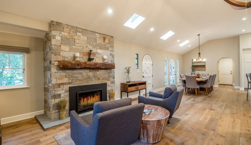 A spacious living room with a stone fireplace, comfortable seating, and a dining area with a chandelier.