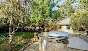An outdoor kitchen area with a built-in grill, stone walls, and a patio with outdoor furniture.