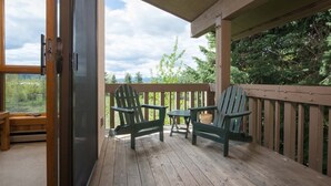 A wooden deck with two Adirondack chairs and a small table, overlooking a forested area.