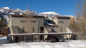A two-story building with a covered parking area and a mountain backdrop. - JHRL - Mtn Alder 824, A cozy 2 bedroom condominium located in The Aspens (Wilson)