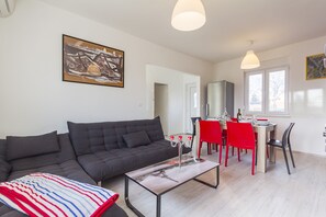 Ein modernes Wohnzimmer mit einem dunkelgrauen Sofa, einer gestreiften Decke, einem Glastisch und einem Essbereich mit roten Stühlen und einem Holztisch.
