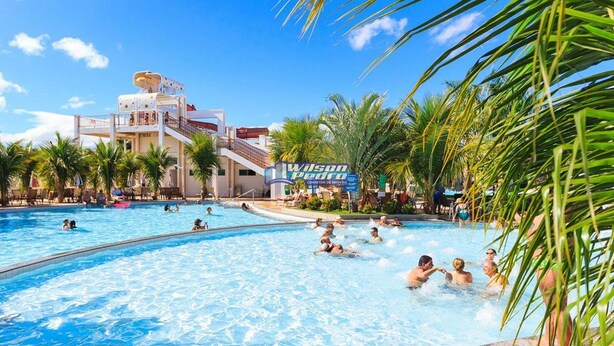 Een hotel zwembadgedeelte met meerdere zwembaden, palmbomen en een gebouw met een bord waarop 'Wilson Pedro' staat.