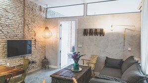 Un soggiorno con parete in pietra, tavolino in legno, divano, televisione e una porta che dà all'esterno.