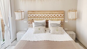 Una camera da letto con testiera in legno, biancheria da letto bianca e lampadario appeso in vimini.