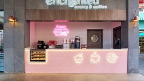 Una panadería y cafetería llamada 'enchanted', con un letrero de neón, una barra llena de pasteles y una máquina de café.